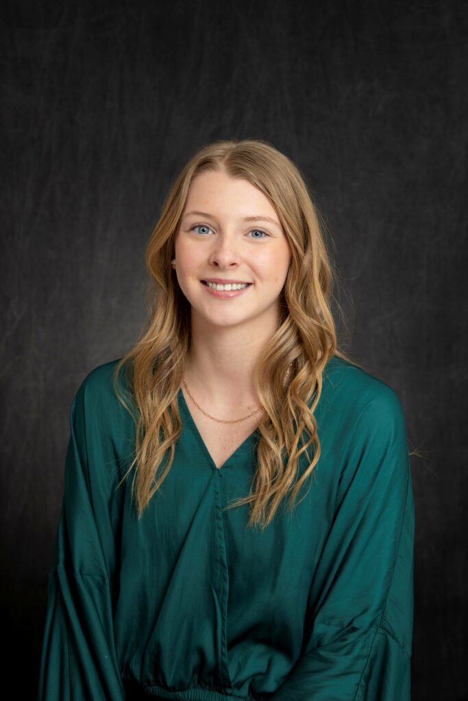 a young white woman with strawberry blonde hair wearing a green blouse smiles for a professional photograph